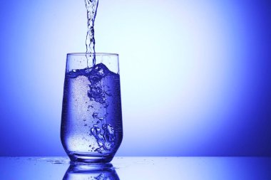 Serinletici gazoz suyunu mavi arka planda cama döküyorum, yakın plan. Metin için boşluk