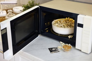 Mikrodalga fırını, patlamış mısır kasesi, çekirdekler ve beyaz mermer tezgahta torba, mutfakta.