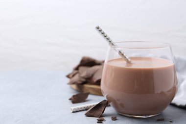 Bardakta çikolatalı süt ve açık gri masada çikolata parçaları, yakın plan. Metin için boşluk