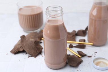 Cam şişelerde çikolatalı süt ve beyaz fayanslı masada çikolata parçaları, yakın plan.