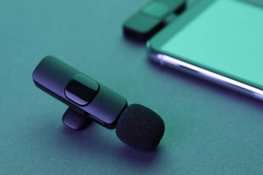 Lavalier mikrofon ve kablosuz alıcısı olan akıllı telefon karanlık masada neon ışıklarda, yakın plan.