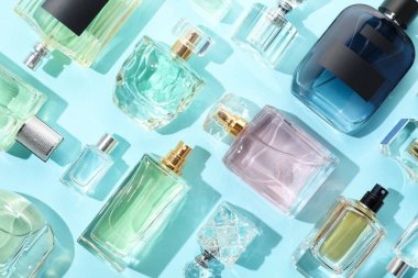 Bottles of various perfumes on light blue background, flat lay