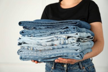 Kapalı alandaki aydınlık duvarın yanında farklı şık kot pantolonları olan kadın, yakın plan.