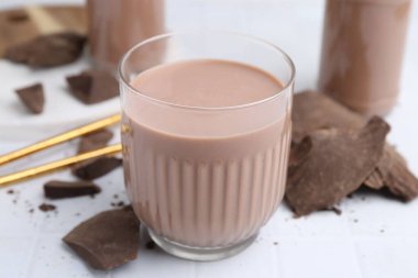 Bardakta çikolatalı süt ve beyaz fayanslı masada çikolata parçaları, yakın plan.