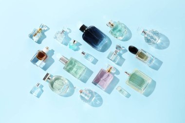 Bottles of various perfumes on light blue background, flat lay