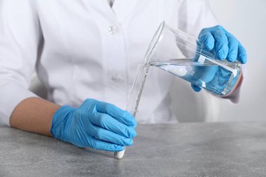 Laboratuvar testi. Bilim adamı deney tüpüne sıvı döküyor. Kapalı alandaki gri masada, yakın plan.