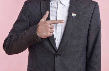 Açık pembe arkaplanda LGBT bayrağı renginde kalp şeklinde iğnesi olan adam, yakın plan