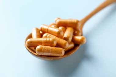 Açık mavi arkaplandaki ahşap kaşıkta zerdeçal kapsülleri, yakın plan