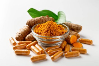 Beyaz arka planda zerdeçal kapsülleri, toz, kökler ve yeşil yapraklar, yakın plan