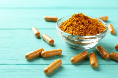 Turkuaz ahşap masa üzerinde zerdeçal kapsülleri ve toz, yakın plan. Metin için boşluk