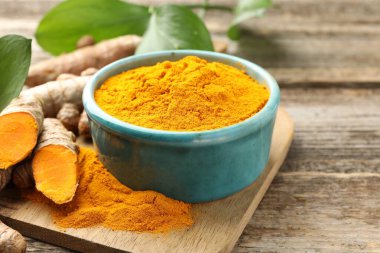 Tabakta zerdeçal tozu, kökler ve yapraklar ahşap masada, yakın plan.