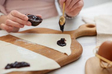 Beyaz masada taze hamur üzerine reçel döken bir kadın, yakın plan. Kruvasan yapıyorum.