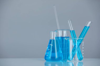 Aynanın yüzeyinde gri arka planda mavi sıvı bulunan laboratuvar camları. Metin için boşluk