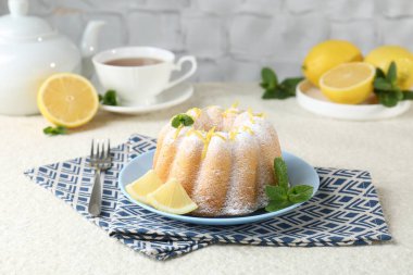 Limon aromalı lezzetli pasta, pudra şekeri ve hafif desenli masada nane şekeri.