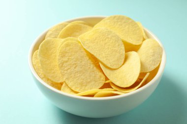 Açık mavi arka planda, kasede patates cipsi, yakın plan.
