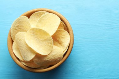 Açık mavi ahşap masada, tabakta patates cipsi, üst manzara. Metin için boşluk