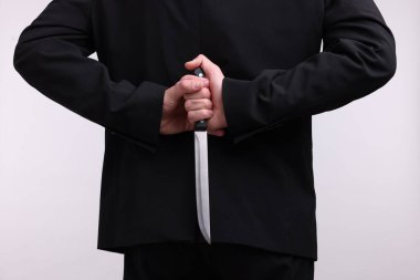 Beyaz arka planda sırtında bıçak tutan iş adamı, yakın plan.