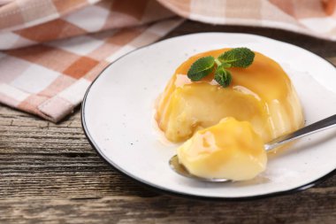 Karamel soslu lezzetli puding ve ahşap masada servis edilen nane, yakın plan.