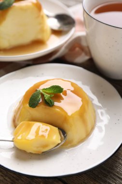 Karamel soslu lezzetli puding ve ahşap masada servis edilen nane, yakın plan.