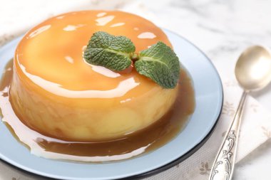 Karamel soslu lezzetli puding ve beyaz masada nane şekeri, yakın plan.