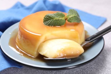 Karamel soslu lezzetli puding, gri desenli masada nane ve kaşık, yakın plan.