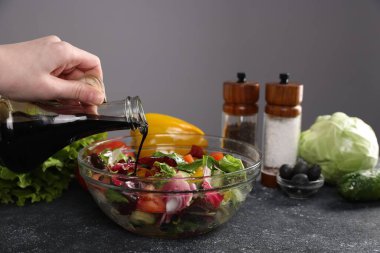 Koyu dokulu masada salataya balzamik sirke döken kadın, yakın plan, gri arka plan...