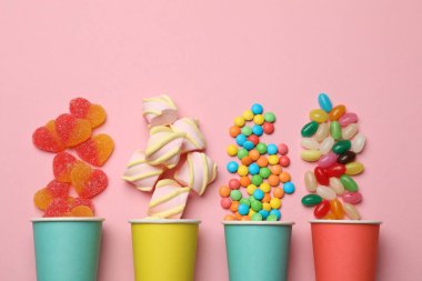 Lezzetli şekerler, marşmelovlar ve pembe arka planda kağıt bardaklar. Metin için boşluk