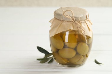 Cam kavanozda yeşil zeytin turşusu ve beyaz ahşap masada yapraklar, yakın plan. Metin için boşluk