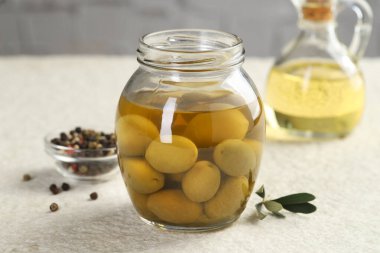 Kavanozda turşulu yeşil zeytin, beyaz desenli masada yağlı ve biberli mısır, yakın plan.