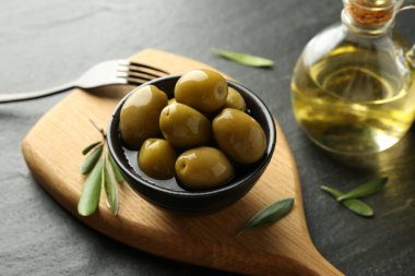 Lezzetli marine edilmiş zeytinler kasede, yeşil yapraklar ve yağ siyah masada, yakın plan.