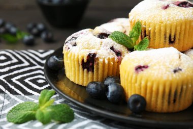 Yaban mersinli lezzetli çörekler, pudra şekeri ve nane şekeri siyah masada, yakın plan.