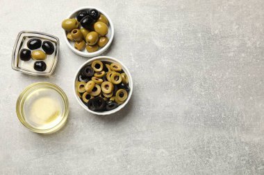 Farklı lezzetlerde marine edilmiş zeytin halkaları, hepsi ve gri desenli masa üzerindeki yağ, düz yatak. Metin için boşluk