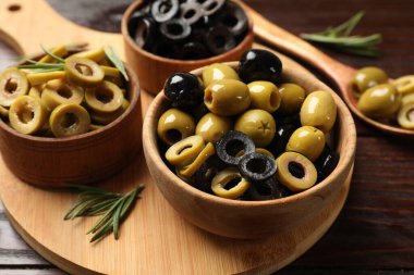 Farklı lezzetlerde marine edilmiş zeytin halkaları, tüm olanlar ve ahşap masada biberiye, yakın plan.