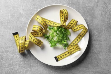 Bulimia. Tabak, salata ve ölçü bandı gri masa, üst görünüm