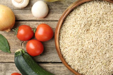 Tabaktaki çiğ kahverengi pirinç taze ürünlerin arasında, ahşap masada, düz yerde.