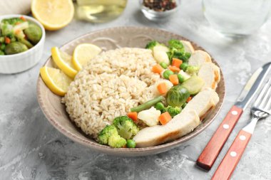 Gri desenli masada servis edilen tavuk, sebze ve limon dilimleri ile nefis kahverengi pirinç, yakın plan.