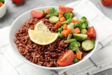 Gri masada servis edilen sebzeli ve limon dilimli lezzetli kahverengi pirinç, yakın plan.