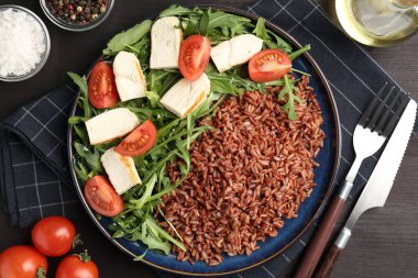 Siyah ahşap masada servis edilen tavuk, roka ve domatesli leziz kahverengi pirinç, düz yatıyordu.