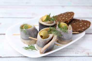 Zeytinli lezzetli ringa dürümleri, beyaz ahşap masada dereotu ve ekmek, yakın plan.