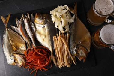 Farklı kurutulmuş balık atıştırmalıkları ve bira siyah masanın üstünde.