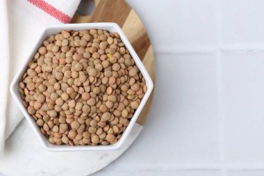 Beyaz fayanslı masa üzerinde çiğ kahverengi mercimek, üst manzara. Metin için boşluk