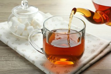 Tahta masada çaydanlıktan fincana taze demlenmiş çay dökülüyor, yakın plan.