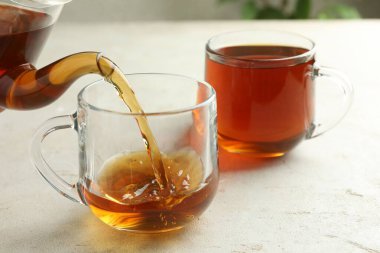 Hafif desenli masada çaydanlıktan fincana aromatik çay dökülüyor, yakın plan.