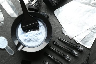 Beyazlatıcı toz ve kuaför aletleri siyah masada, düz yerde.