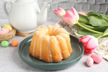 Lezzetli kek, paskalya yumurtaları ve laleler gri masada, yakın plan.