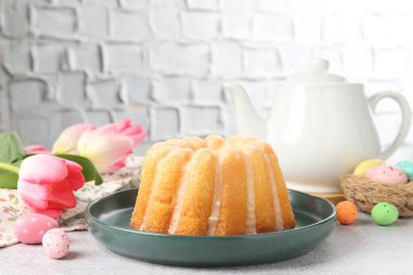 Lezzetli kek, paskalya yumurtaları ve laleler gri masada, yakın plan.