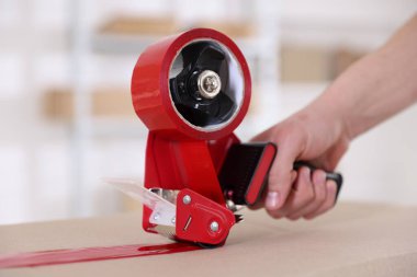 Karton kutuyu kapalı bir yere kapatmak için yapıştırıcılı bant kullanan bir adam.