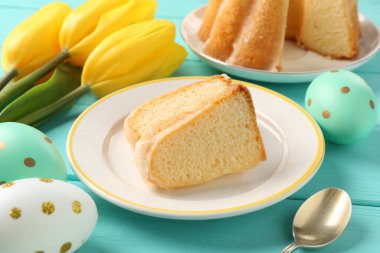 Lezzetli kek parçaları, paskalya yumurtaları ve laleler açık mavi ahşap masada, yakın plan.