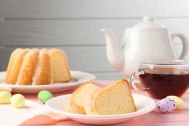 Lezzetli kek parçaları, pembe ahşap masada paskalya yumurtası ve çay.
