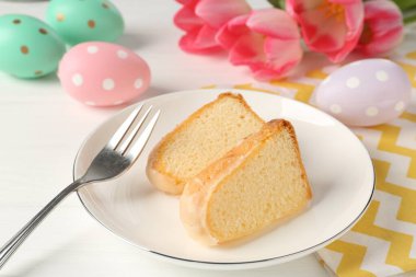 Lezzetli kek parçaları, beyaz ahşap masada paskalya yumurtası ve laleler, yakın plan.